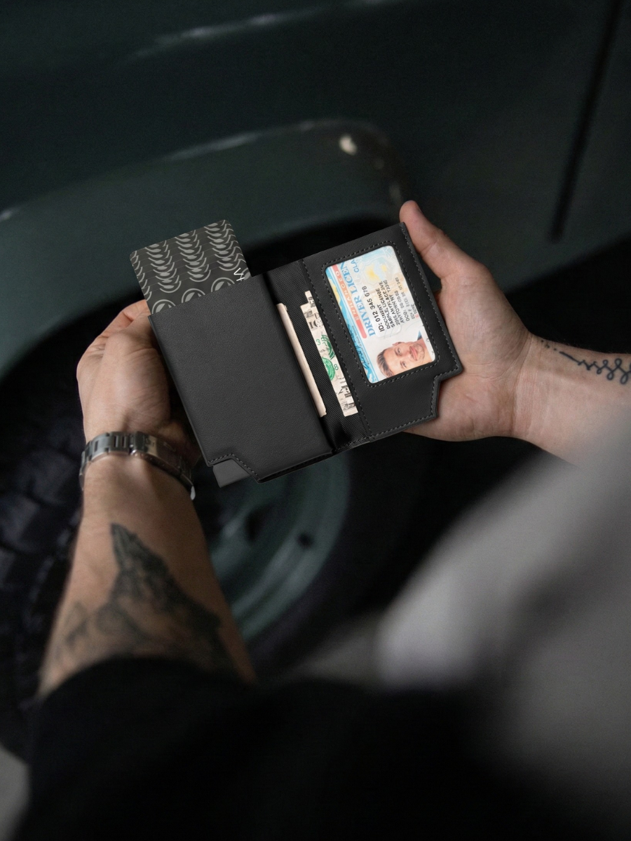 Person holding a black wallet with various cards and a ID card, sitting on a dark surface.