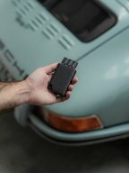 Hand holding a black wallet in front of a vintage car